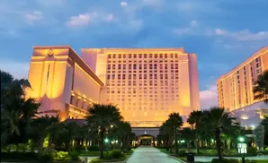 A grand hotel at twilight, illuminated with warm lights, with palm trees in the foreground.