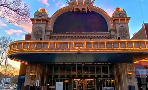 Grand theater facade with arched marquee lit by marquee lights at sunset.