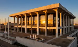 Modern building with large windows reflecting sunset, supported by columns.