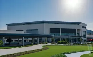 Modern, light-colored office building with a covered walkway and manicured lawns under a bright sun.