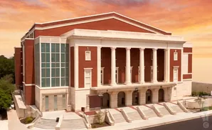 A red brick building with white columns and large windows, set against a colorful sky.