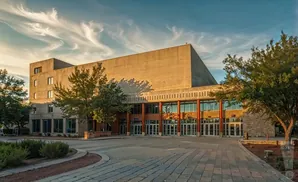 A large brutalist building with a wide paved walkway in front, under a dramatic sky.