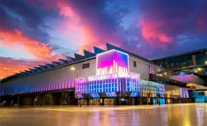 A modern building illuminated with vibrant pink and blue lights under a dramatic sunset sky.
