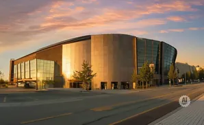 A modern, curved building with glass and tan panels at sunset.