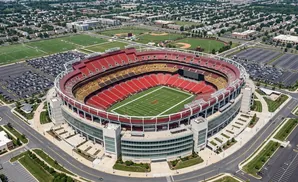Aerial view of a large, red-seated football stadium surrounded by parking lots and residential areas.