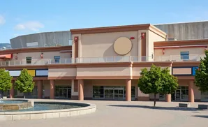 A modern building with a circular sign, balconies, and trees, in front of a fountain.