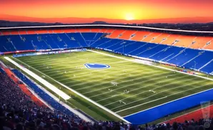An aerial view of a football stadium with blue and orange seats, a green field, and a sunset sky.