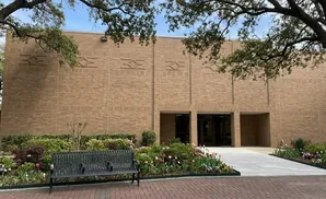 A brick building with patterned accents, a dark bench, and a flowerbed in front.
