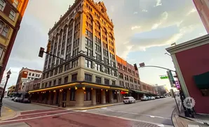 A vintage building with ornate architecture stands tall on a city street corner, illuminated by warm sunlight.