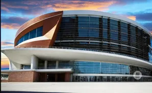 Modern arena with curved glass facade and copper accents under a dramatic sky.