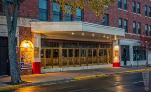 Exterior of a brick building with large wooden doors and windows under a marquee, street in foreground.