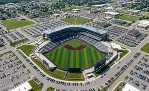 Aerial view of a baseball stadium with a green field and surrounding parking lots, buildings, and residential areas.