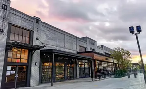 Modern brick building with large windows and outdoor seating under a cloudy sunset sky.