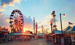 Ferris wheel and rides at a carnival at sunset, with colorful lights and a cloudy sky.