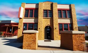 Building with stone facade, red trim windows, and outdoor seating under a colorful sky.