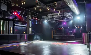 An empty, modern nightclub with a dance floor, bar, and stage lighting.