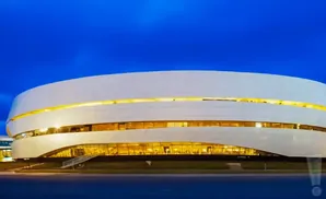 Modern white stadium with glowing yellow accents against a deep blue night sky.