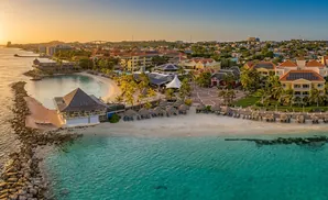 Aerial view of a tropical resort with buildings, beaches, and turquoise water at sunset.