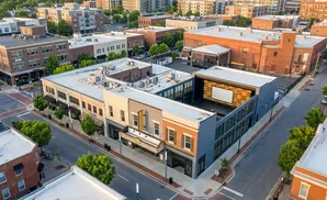 Aerial view of a modern theatre building with a large screen and an outdoor stage, surrounded by brick buildings and trees.