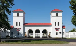 White building with red roofs and two towers, arched entrances, and patriotic bunting.