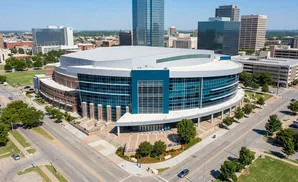 Aerial view of a large, modern arena with a curved glass exterior, surrounded by city buildings and trees.