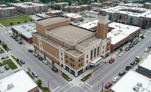 Aerial view of a city street with a large brick theater, apartment buildings, and parked cars.