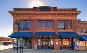 Exterior of a brick building with blue awnings and large windows, featuring a lit street lamp in front.