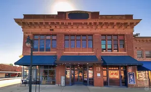 Exterior of a two-story brick building with large windows, blue awnings, and a decorative cornice.