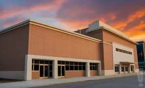 A modern brick building with large windows and a dramatic sunset sky.
