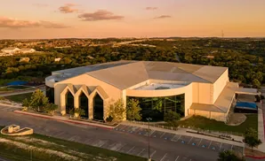 Aerial view of a large modern building with a silver roof and tan exterior walls during sunset.