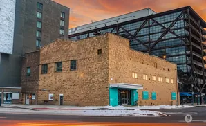 Brick building with a modern glass structure behind it, under a sunset sky.