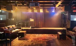 Stage and seating area in a dimly lit club with a leather couch and ottomans on a tiled floor.