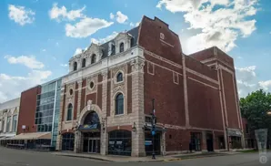 Building with ornate stone facade and brick addition under a cloudy sky.