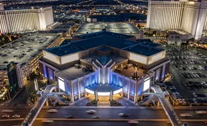 Aerial view of a large hotel and casino complex at night, with a parking lot filled with cars and a statue of Elvis Presley.