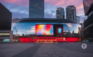 A modern arena with a large digital screen displays abstract art, reflecting city lights under a twilight sky.