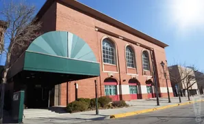 Brick building with a green awning over an entrance. Arched windows with white panes are visible.