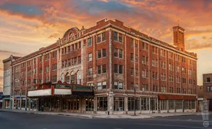 An old brick theater building with a marquee and shops at sunset.