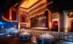 Elegant theater with a stage, red curtains, and tables set for a banquet.