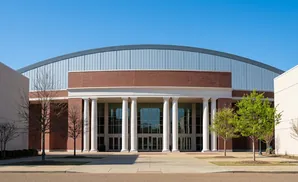 Front view of a building with a curved metallic roof, brick facade, and a colonnade entrance.