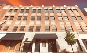 Red brick building with arched windows and awnings over storefronts. A small tree stands in front.