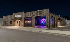Exterior of a rustic wooden building at night, with garage doors open to reveal a lit stage.