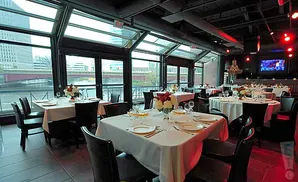 Tables set for dining in a restaurant with large windows overlooking a river and city skyline.