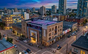 Exterior view of a city block at dusk with illuminated buildings and streetlights.