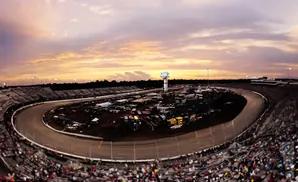 A panoramic view of a race track at sunset with spectators in the stands.