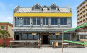 Beachfront building with a yellow awning, wooden deck, and volleyball net.