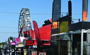 Ferris wheel and colorful carnival rides and food stalls under a clear blue sky.