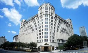A grand, cream-colored building with many windows, under a blue sky with white clouds.