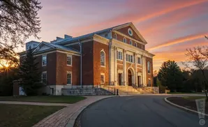 A grand brick building with classical columns at its entrance, bathed in the warm glow of a sunset.