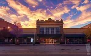 A theater facade with decorative details and a clock, set against a vibrant sunset sky with wispy clouds.