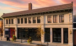 Exterior of a historic building with a tiled roof, large windows, and a brick chimney, at sunset.